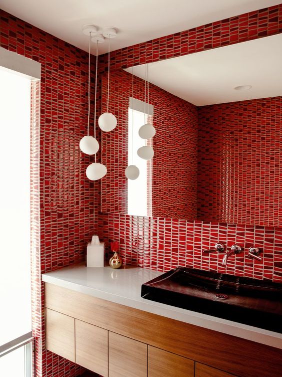 a bright red bathroom clad with bold mosaic tiles, a dark sink and pendant lamps