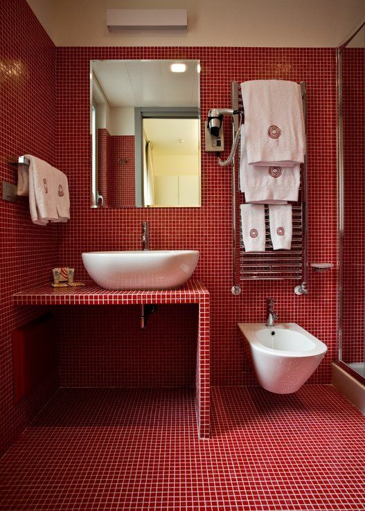 a bright red bathroom fully clad with tiles including the shower space and vanity, with white appliances and white towels