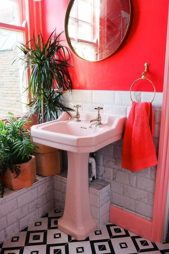 a bright red bathroom with white marble tiles, a white sink, mosaic tiles on the floor and potted plants to refresh the space