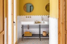 a chic bathroom with mustard walls, white herringbone tiles, a double vanity with bowl sinks and round mirrors