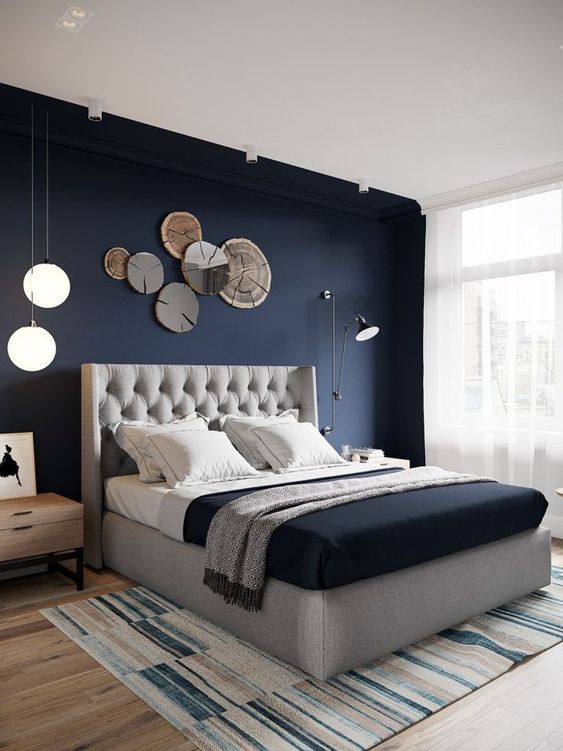 a chic bedroom with a navy statement wall, a grey upholstered bed, some catchy lights and lamps