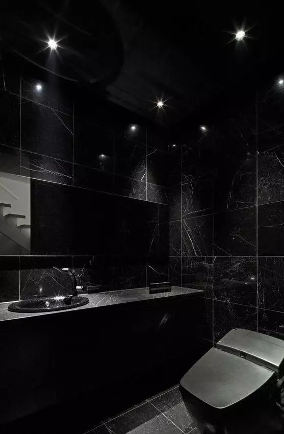 a chic black bathroom with blakc marble tiles and a black marble vanity plus a black toilet