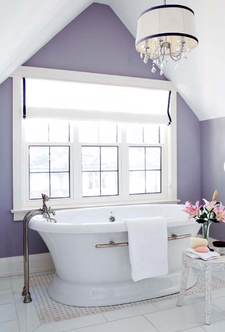 A chic vintage inspired bathroom with purple walls, a gorgeous comfy bathtub and an elegant chandelier