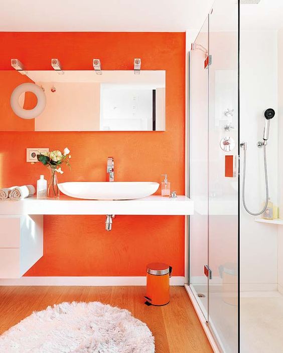 a contemporary bathroom with an orange statement wall, a matching trash can and some hardware plus refreshing whites