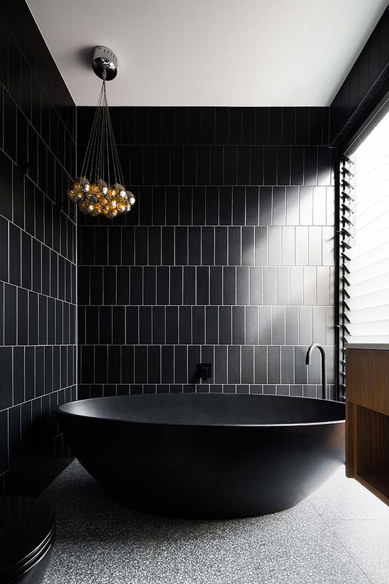 a contemporary black bathroom clad with skinny tiles, a terrazzo floor, a glazed wall and a cluster of pendant lamps