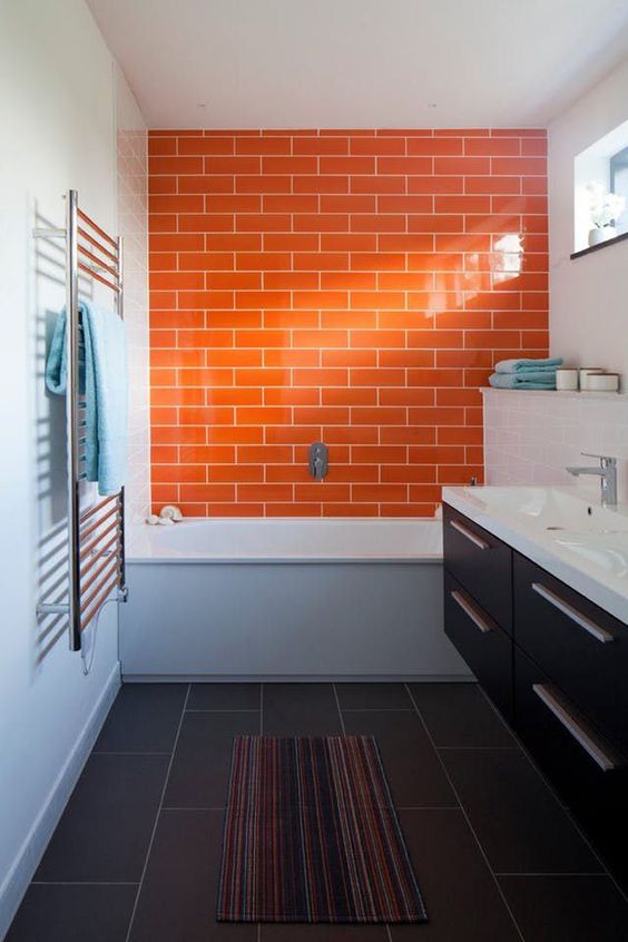 a contrasting grey and white bathroom is accented with a dark stained floating vanity and a bright orange tile wall