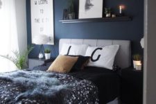 a grey and navy bedroom with a statement wall, a grey upholstered bed and nightstands, some modern artworks