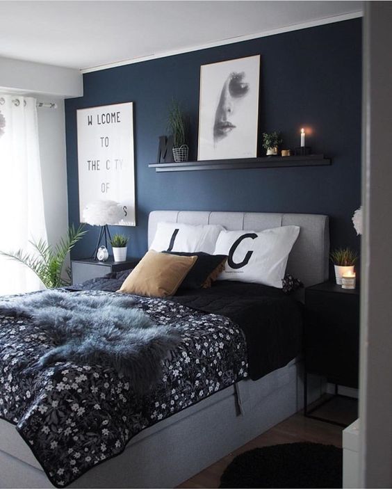 a grey and navy bedroom with a statement wall, a grey upholstered bed and nightstands, some modern artworks