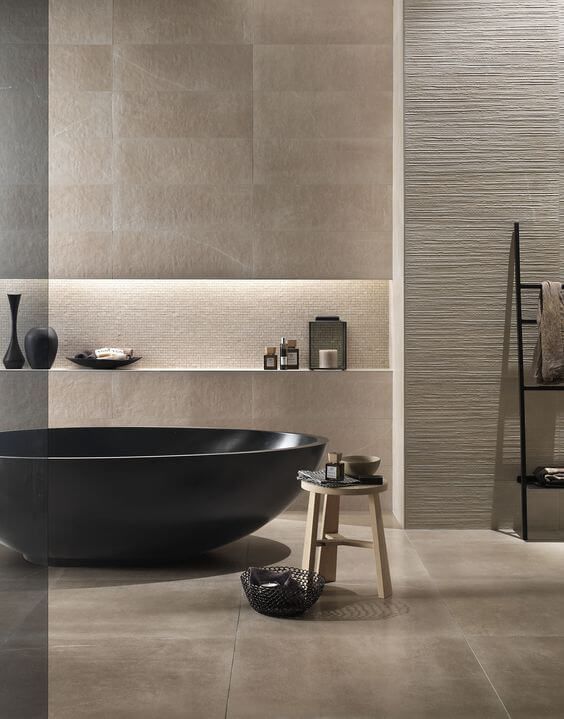 a luxurious beige bathroom with tiles and textural wall panels, a dakr bathtub and lots of bowls and cups