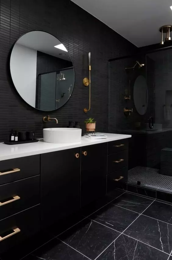 a modern black bathroom with skinny and black marble tiles, a large black vanity, a shower space and a round mirror