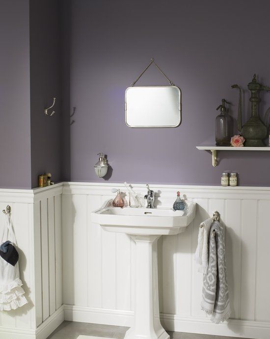 A moody modern farmhouse bathroom with purple walls, white paneling, a free standing sink and vintage shelves