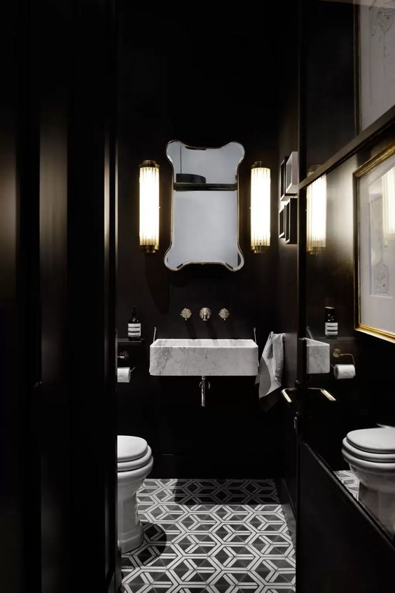 a moody vintage bathroom with black walls, a white floating sink, a catchy mirror and wall sconces and white applainces