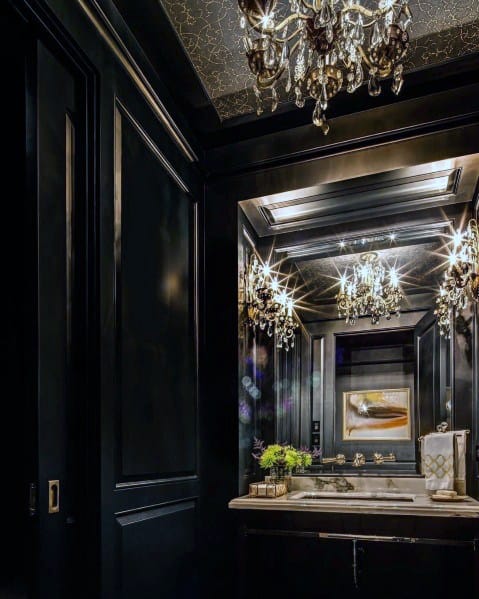 a refined black bathroom with a black and gold ceiling, a mirror, a black vanity, a chic chandelier and black paneling on the walls