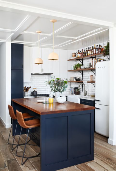 a small farmhouse kitchen in white and navy, with a kitchen island with a stained countertop, pendant lamps and a subway tile backsplash