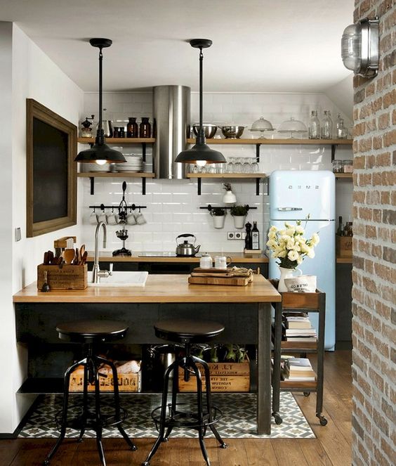 a small industrial kitchen with blackcabinets and a kitchen island plus butcherblock countertops, black pendant lamps and a blue fridge