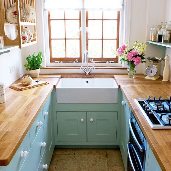 a small pastel farmhouse kitchen with mint cabients, butcherblock countertops, wooden open shelves and a window with wooden framing