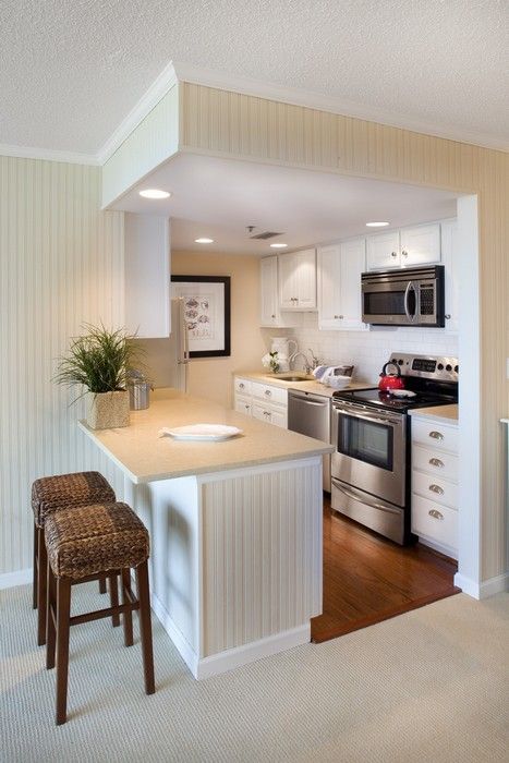A small traditional kitchen in off white placed into a cube, with a kitchen island that separates the spaces