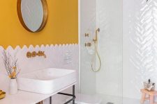 a stylish bathroom with a sunny yellow wall, white tiles, a round mirror and a neutral and lighweight vanity