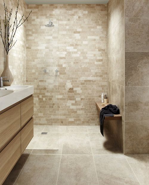 a tan and taupe bathroom clad with tiles of various sizes, a beige vanity and white sinks
