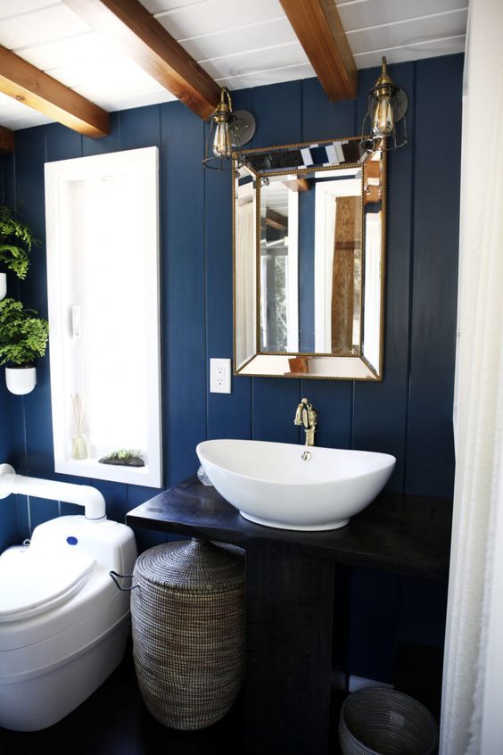 a tiny bathroom done with blue painted wood, wooden beams on the ceiling and a basket for storage