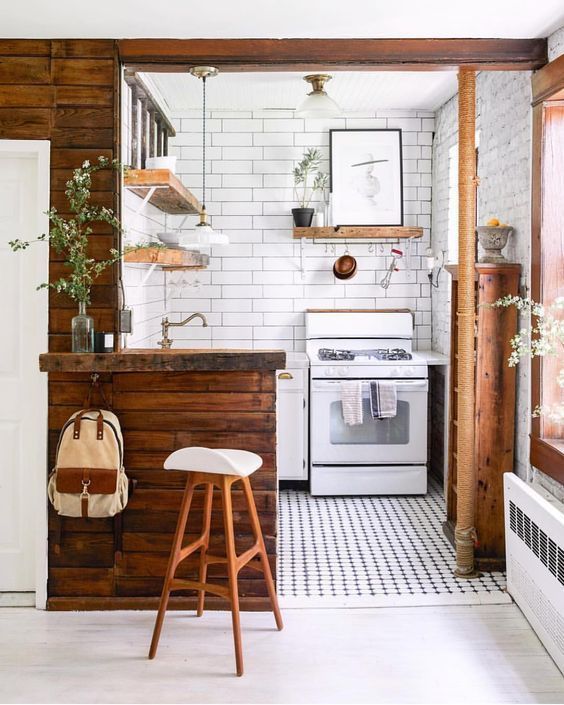 A tiny kitchen done in white and with rich stained wooden surfaces, potted greenery and a mosaic tile floor
