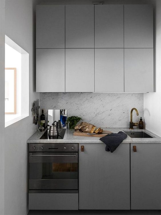 a tiny minimalist kitchen with sleke grey cabinets, leather pulls and a grey stone backsplash