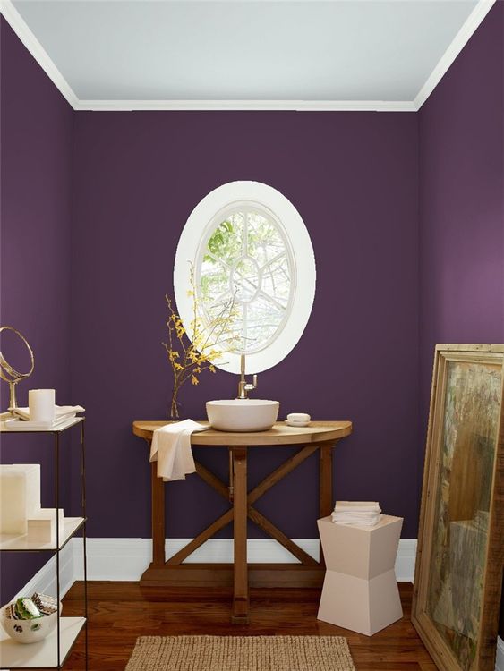 a unique purple bathroom with an oval framed window, a wooden vanity and a vessel sink, an etagere and an artwork
