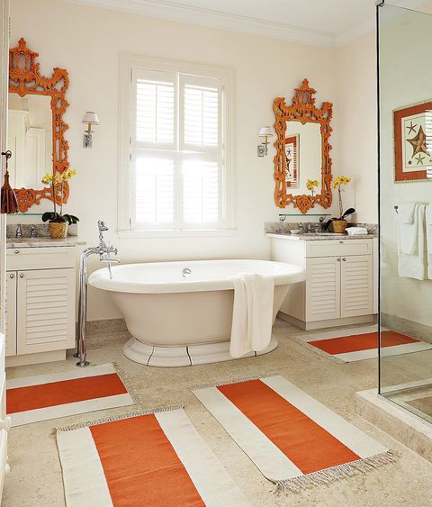 a vintage-inspired bathroom done in neutrals and accented with orange ornate mirrors and striped rugs