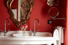 a vintage red powder room with red walls, an antique white vanity with sinks and exquisite mirrors