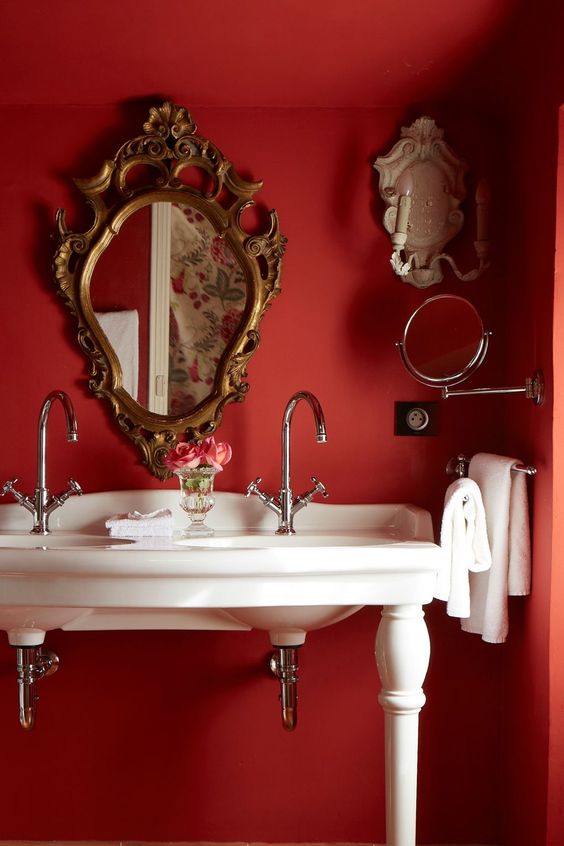 a vintage red powder room with red walls, an antique white vanity with sinks and exquisite mirrors