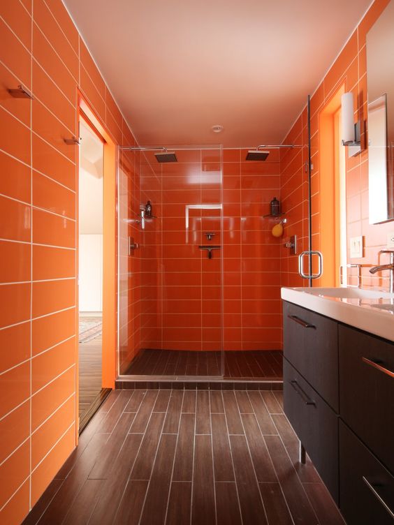 a warm bathroom with orange tile walls and wood-inspired tiles on the floor for a bright and welcoming space