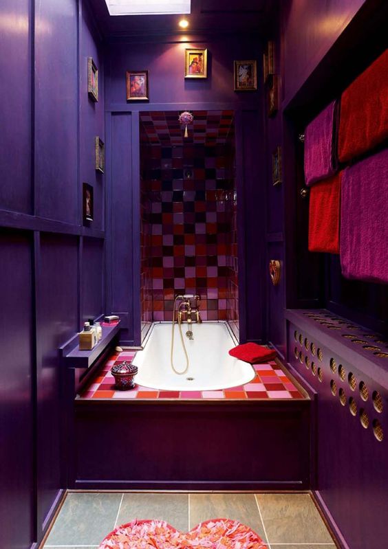 a whimsical Moroccan-inspired bathroom with purple and aubergine walls, bright mosaic tiles, a gallery wall and a heart-shaped rug