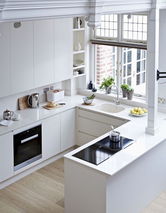 A white minimalist kitchen with sleek cabinets, no handles, a window and simple built in appliances