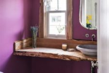 an eclectic bathroom with purple walls, a wooden vanity with a livign edge, a crystal chandelier and a lavender vessel sink