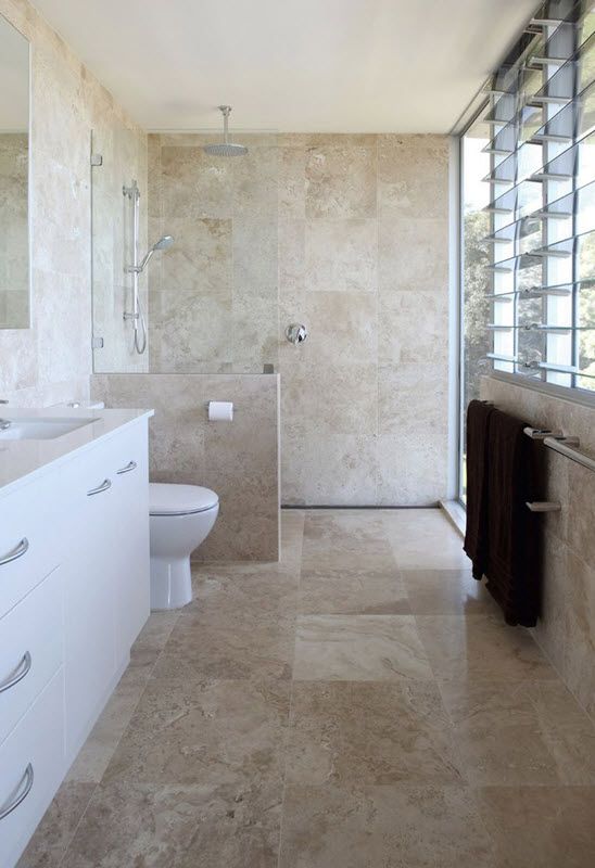 Beige stone inspired tiles covering the whole bathroom, white items and a vanity for an elegant look