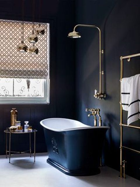 navy painted bathroom walls, a navy bathtub, pritned Roman shades, pendant lamps and a side table