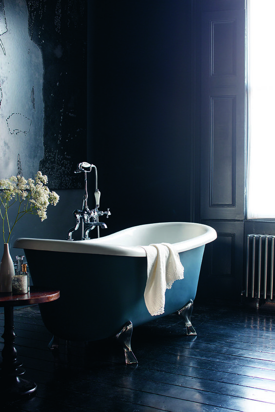 navy walls and a navy wooden floor, a navy clawfoot bathtub, a side table plus shutters show off refined vintage