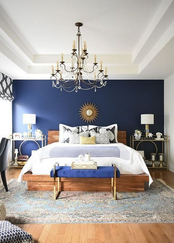 a boho glam bedroom with a navy statement wall and bench, a crystal chandelier, creative nightstands and candles