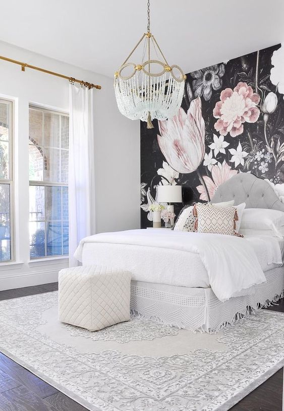 a contemporary glam bedroom with a statement floral wall, a crystal chandelier, a white ottoman and a printed rug