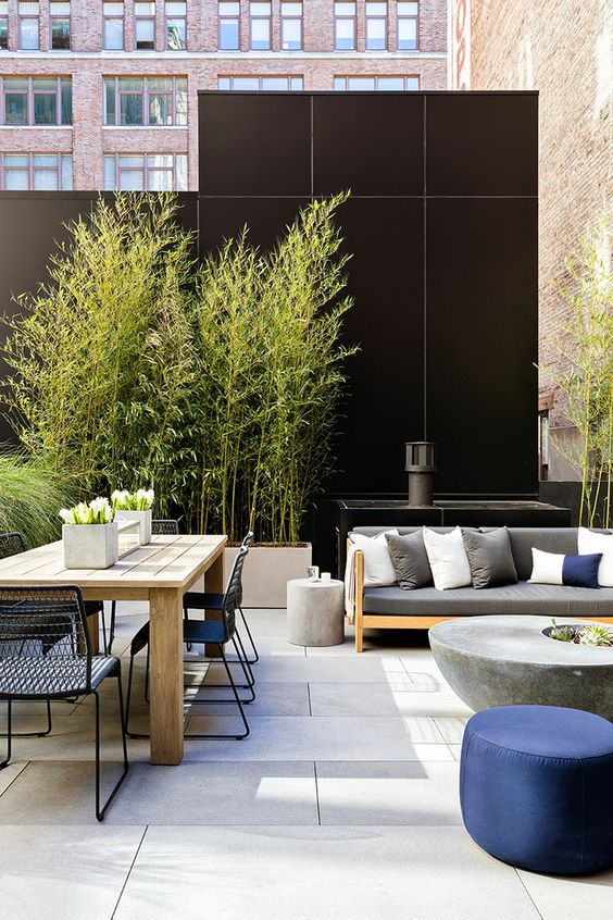 a cool modern terrace with simple furniture, a concrete table, a wooden dining table and metal chairs plus potted greenery