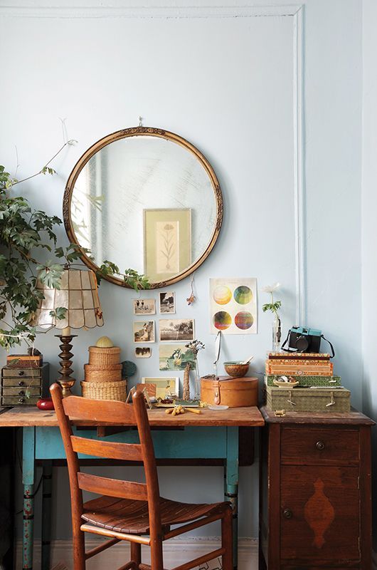 a cute vintage working nook with a vintage desk, chair and a cabinet, a mirror in a vintage gilded frame, greenery and some art