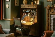 a fab vintage working nook with a stained bureau desk, a table lamp, a green leather chair and some artwork