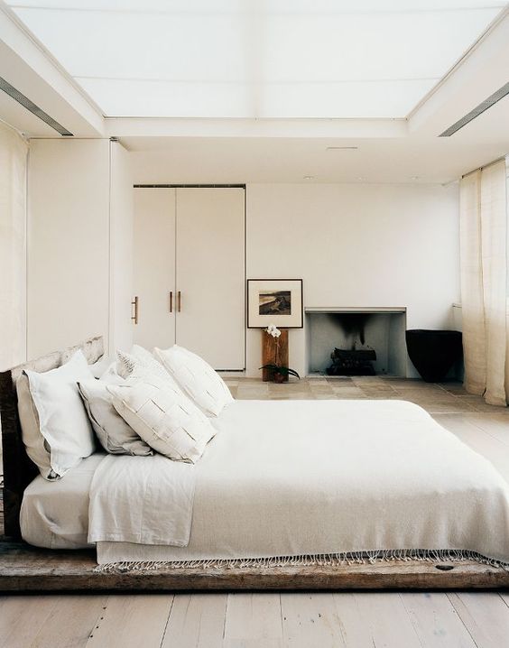 A low key zen bedroom with a bed placed on a wooden platform, exquisite furniture and a built in fireplace, a glazed ceiling