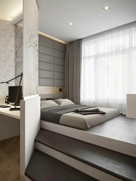 a minimalist and all zen bedroom with a bed placed on a platform, a white nightstand, neutral bedding and an upholstered wall