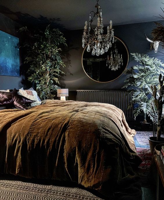 a modern Gothic bedroom with black walls, a bright artwork, a round mirror, a crystal chandelier and potted plants