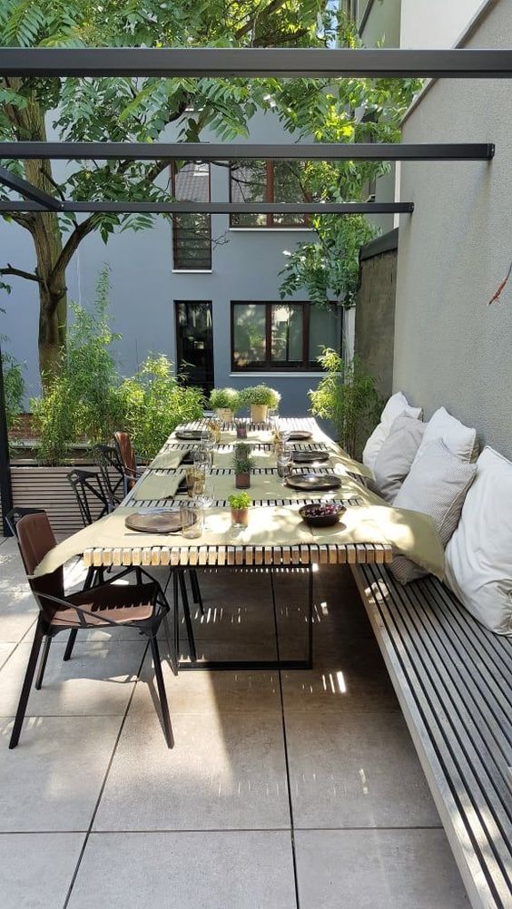 a modern outdoor dining space with built-in benches, a slab table, metal chairs and lots of potted greenery