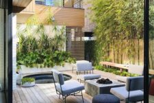 a modern patio with lots of greenery, a hot tub, a concrete firepit, grey chairs and a wicker ottoman