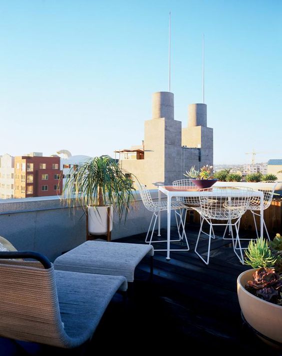 a modern rooftop terrace with a wicker lounger and a footrest, metal furniture, potted plants and a cool view