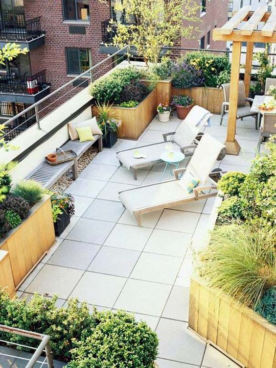 a modern rooftop terrace with loungers, a bench with bright pillows, lots of potted greenery and blooms