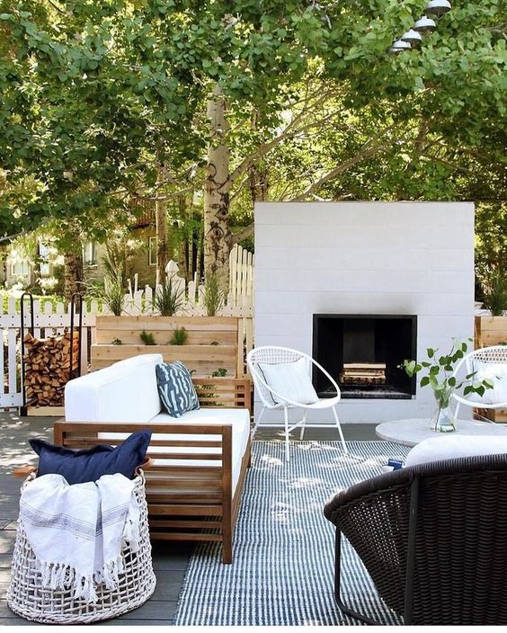 A modern terrace with a built in fireplace, a striped rug, wicker chairs, a wooden sofa and a basket